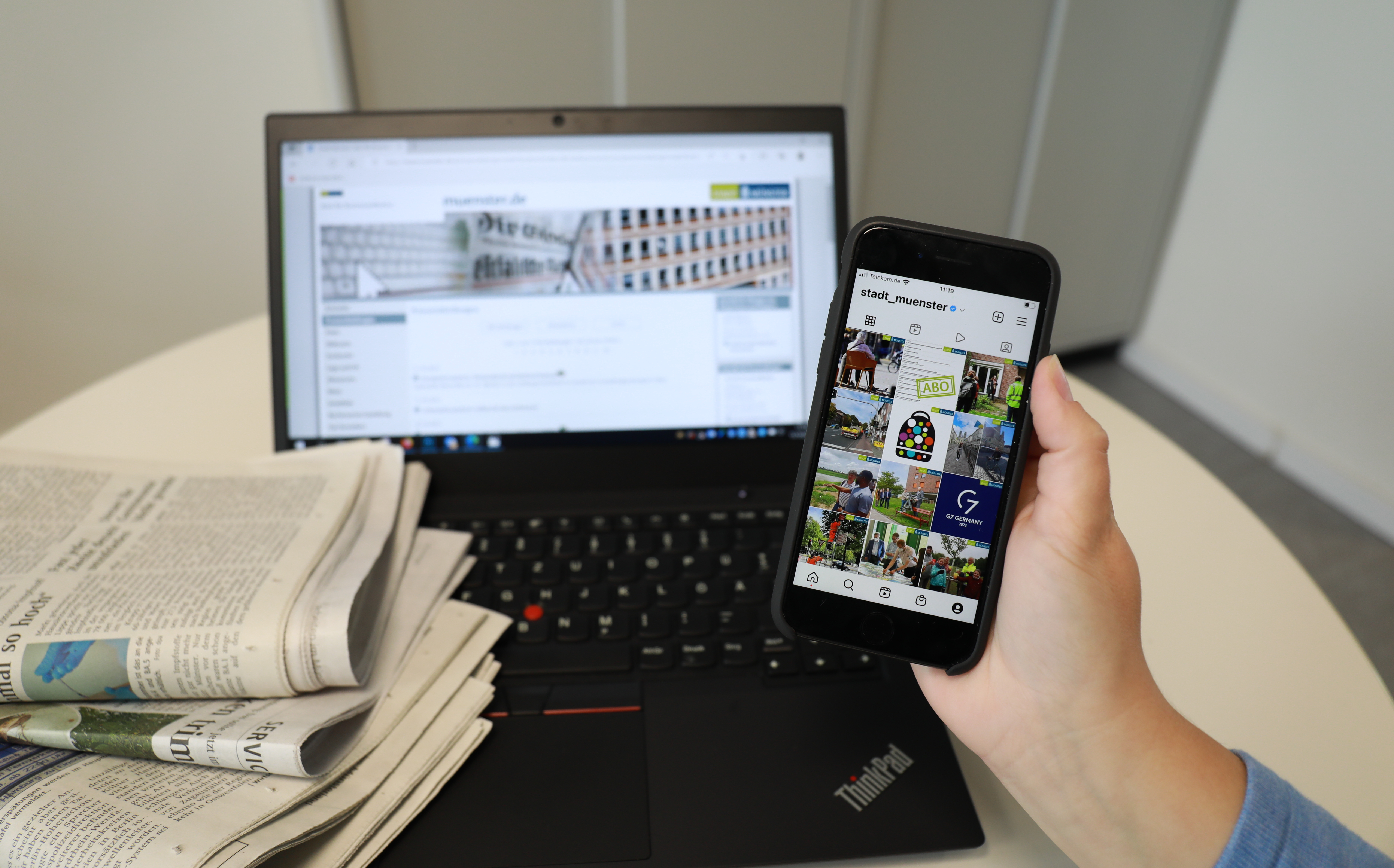 Laptop, Zeitungen und ein Smartphone in der Hand