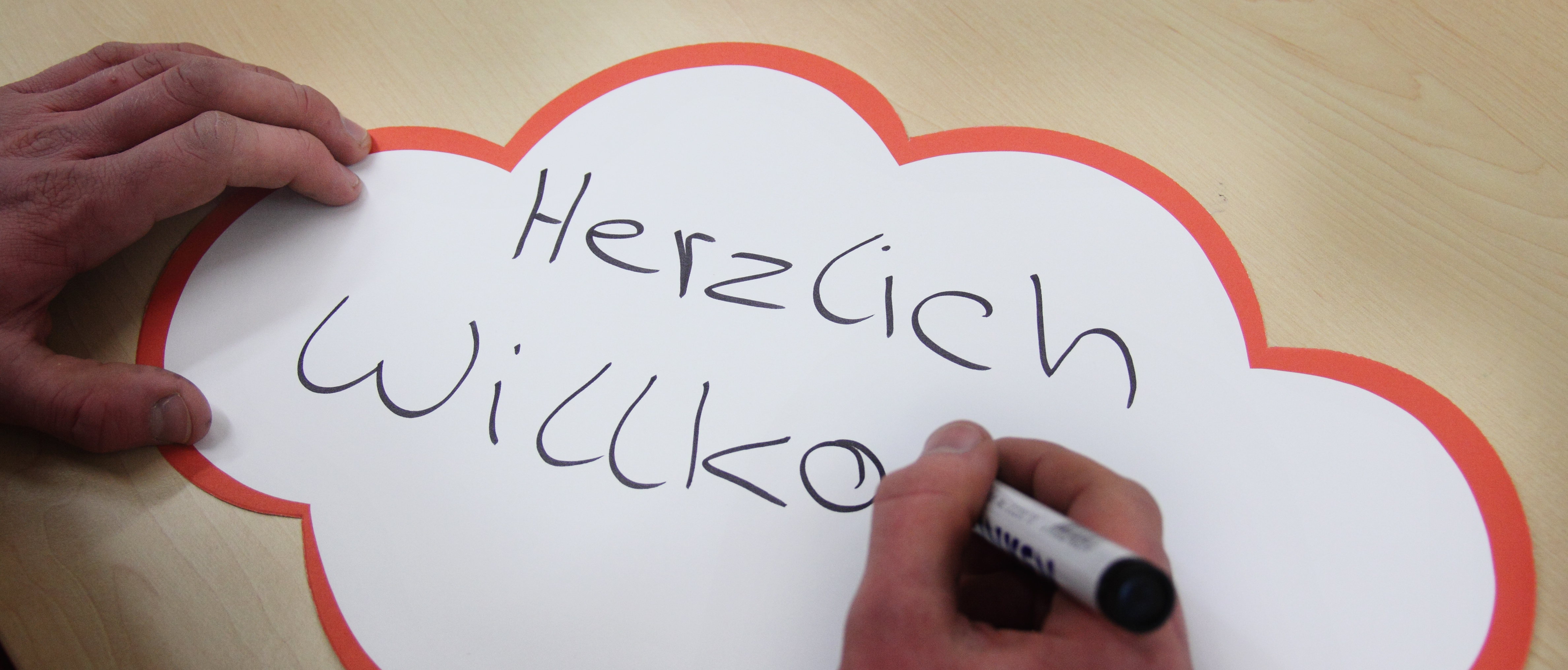 Hände schreiben den Schriftzug "Herzlich willkommen"