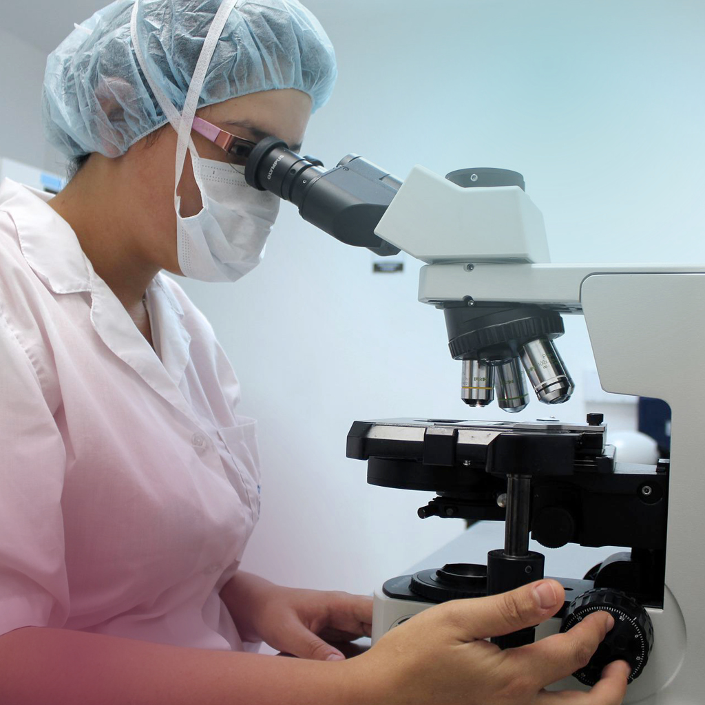 Eine Frau in medizinischer Kleidung arbeitet an einem Mikroskop