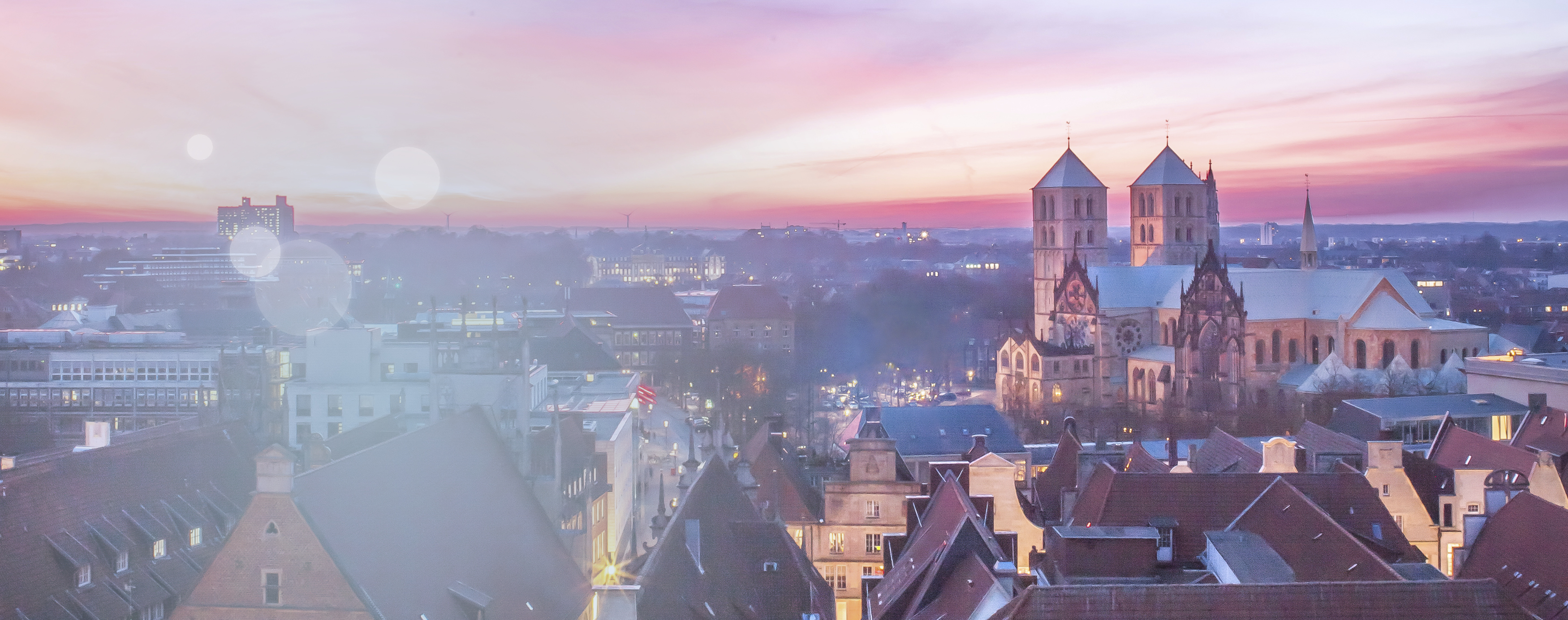 Ein schöner  lila- und rosafarbener Sonnenuntergang aus Sicht des münsterischen Stadthauses zeigt die Dächer von Münster, inklusive des St.-Paulus-Doms.