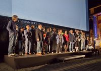 Bei der Open-Air-Premiere von 'Feierstunde' 2016 vor dem Schloß Münster stehen Team und Schauspieler auf der Bühne vor der Leinwand. Foto: Stadt Münster