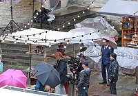 Dreharbeiten im Regen - Schauspieler und Team stehen unter Regenschirmen
