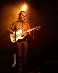Foto zeigt den Musiker Peter Broderick im Scheinwerferlicht auf einer Bühne mit E-Gitarre.