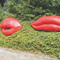 Rote überdimensionale Lippen vor einer Hecke