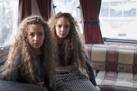 Zwei ähnlich aussehende junge Frauen mit Lockenkopf sitzen in der Polsterecke eines Wohnwagens