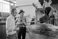 Joseph Beuys mit Hut, Weste und Schaufel steht mit einem Mann in einer Werkstatt an einem großen Bottich