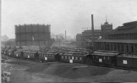 Foto des ehemaligen Güterbahnhofs von 1914: zahlreiche Bahnwaggons hintereinander, im Hintergrund das große Gebäude der städtischen Gasanstalt.