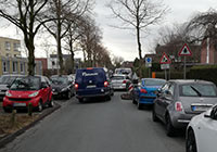 Autos schlängeln sich zwischen parkenden Fahrzeugen durch eine enge Straße.