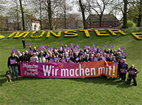 Große Menschengruppe vor dem blühenden Schriftzug 'Münster' an der Promenade