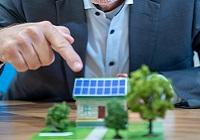 Umweltdezernent Matthias Peck zeigt mit dem Finger auf ein kleines Haus-Modell mit Solaranlage auf dem Dach.