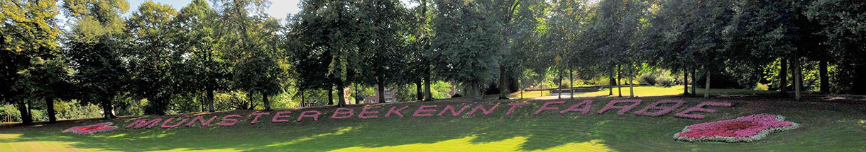 Mit Blumen gepflanzter Schriftzug 'Münster bekennt Farbe' auf einer Rasenfläche an der Promenade