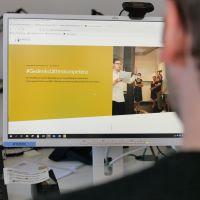 Ein Mann blickt auf einen Computerbildschirm, auf dem die Website von #Gedenkstättenkompetenz aufgerufen ist