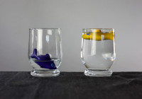Zwei Gläser mit Wasser, in beiden schwimmen Fische. Eines hat wenig Wasser und der Fisch schwimmt ganz unten in einer Pfütze. Eines hat viel Wasser und der Fisch hat viel Platz zum Schwimmen.