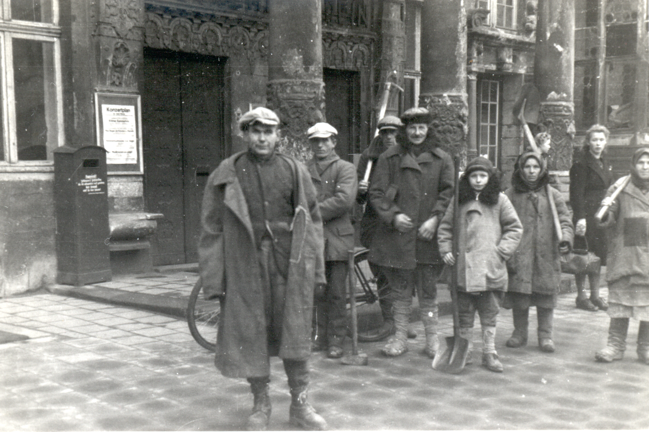 Männer, Frauen und Kinder mit Arbeitsgeräten vor dem Stadtweinhaus