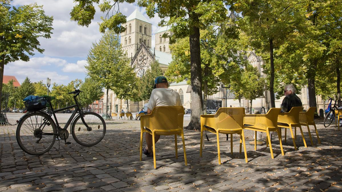 An der Ostseite des Domplatzes, dort, wo sonst entlang der Rückseite der Giebelhäuser Autos parken, stellten Münster Marketing und die Initiative Starke Innenstadt (ISI) 80 Stühle in einem warmen Sandsteingelb auf und luden die Menschen ein, diesen kleinen Teil des zentralen Platzes als "Domplatz-Oase" zu "besetzen".  Die "Domplatz-Oase" war ein Projekt des Zentrenmanagements, gefördert vom Land NRW.