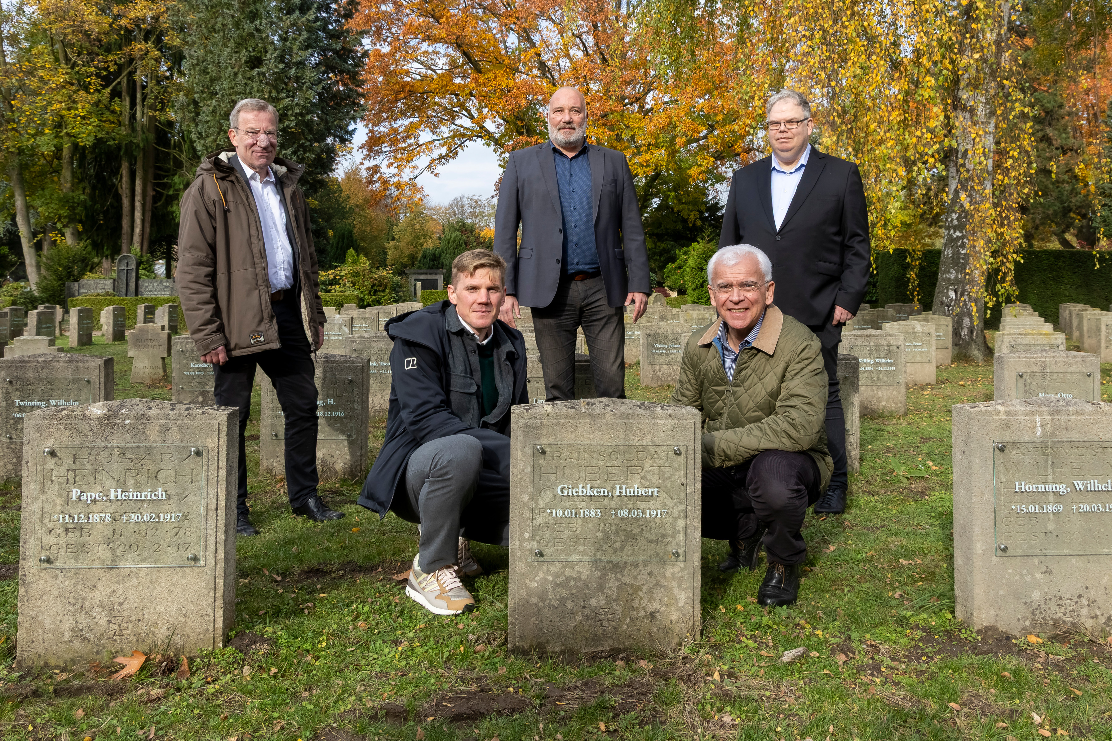 Fünf Männer auf dem Zentralfriedhof neben den Grabsteinen, deren Inschriften erneuert wurden