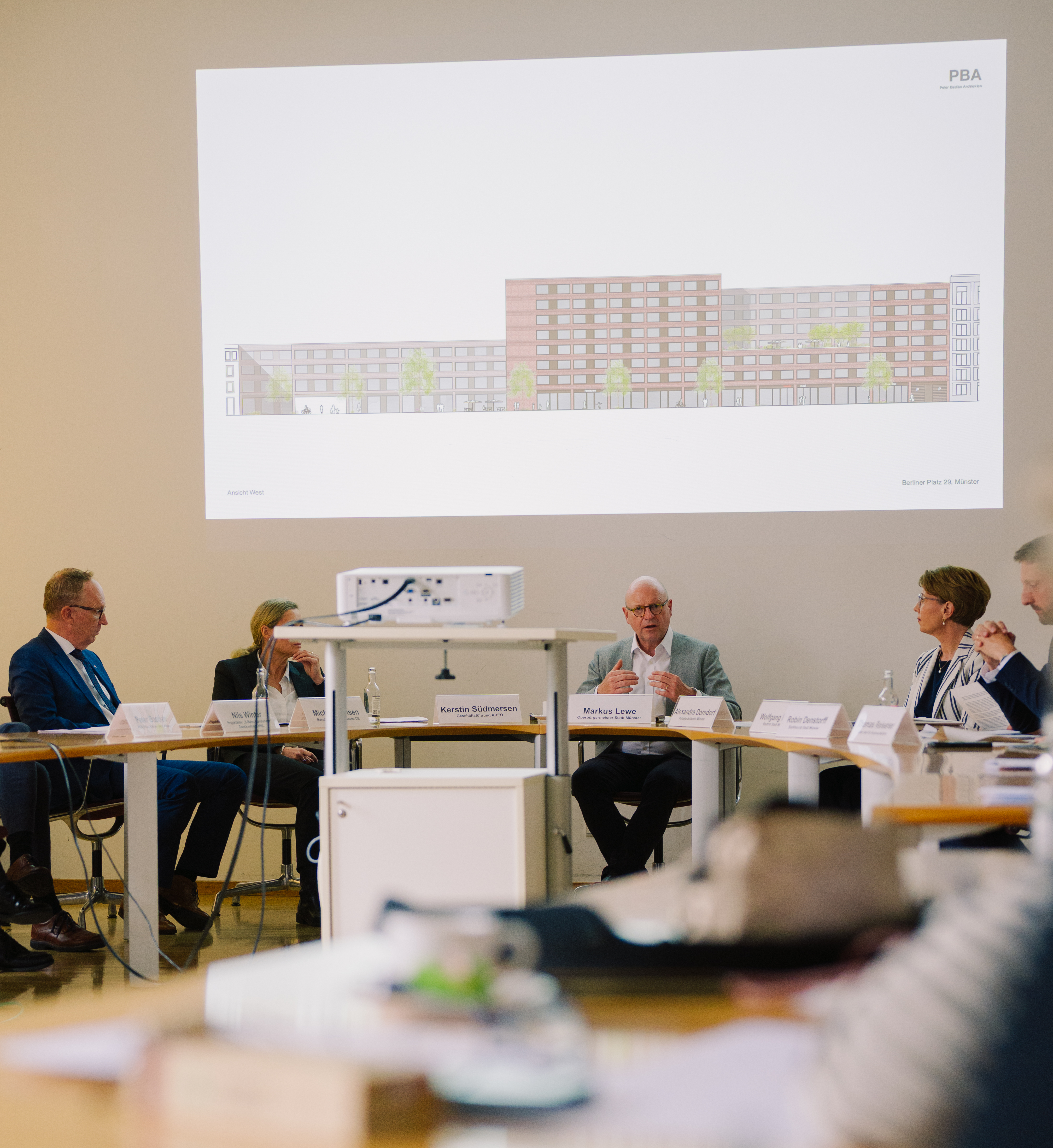 Mehrere Personen am Tisch blicken auf eine Präsentation