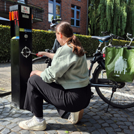 Frau mit Fahrrad benutzt die Radservicestation an der Bismarckallee in Benutzung