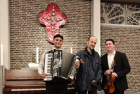 Das Trio PASSIO: v.l. Christian Kurumlian, Piotr Rangno, Leonardo Kurumlian (Foto: Piotr Rangno) Das Trio PASSIO steht vor einer Backsteinmauer in einer Kirche und lächelt in die Kamera.