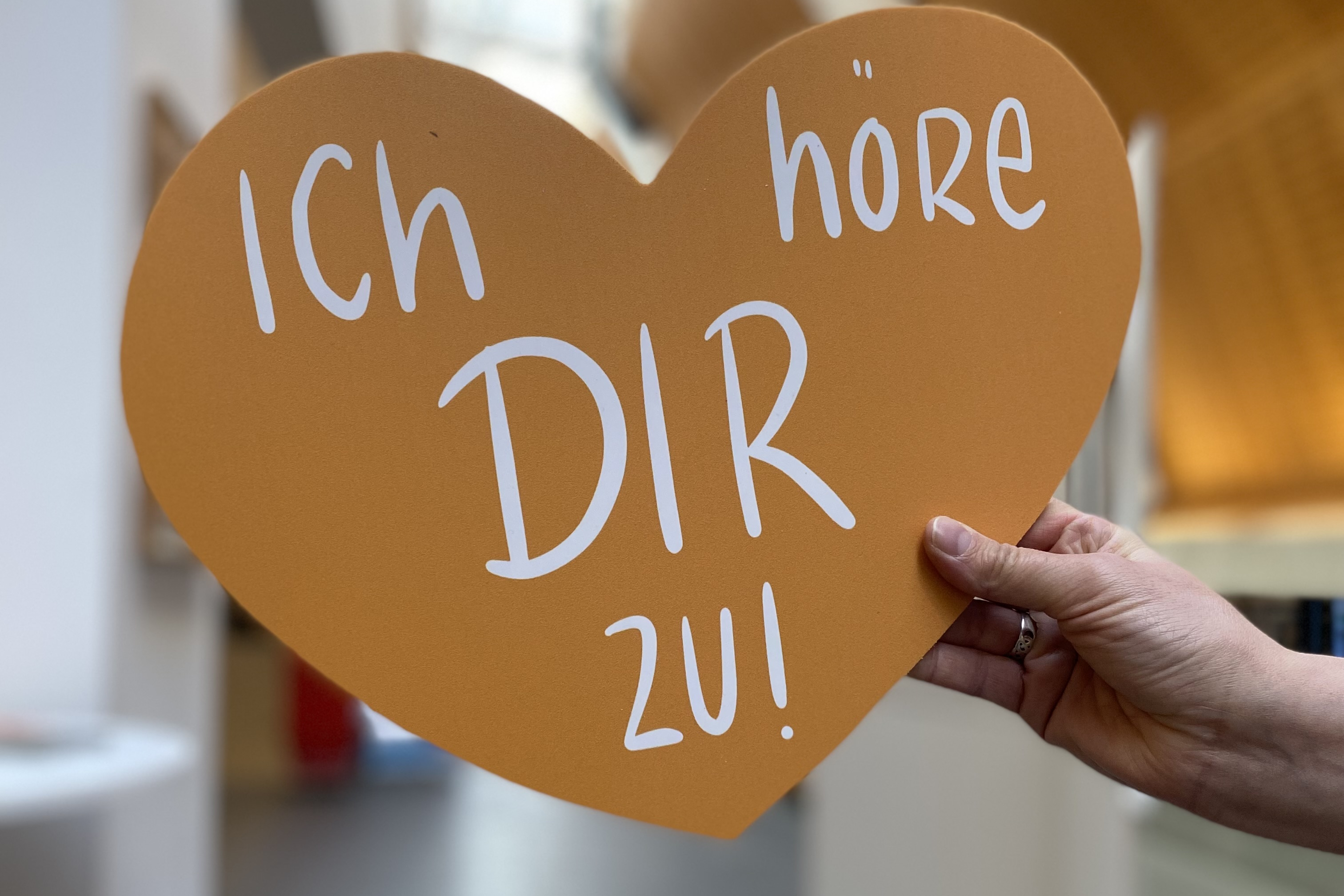 Eine Hand hält ein Herz. Darauf steht der Satz: Ich höre dir zu.