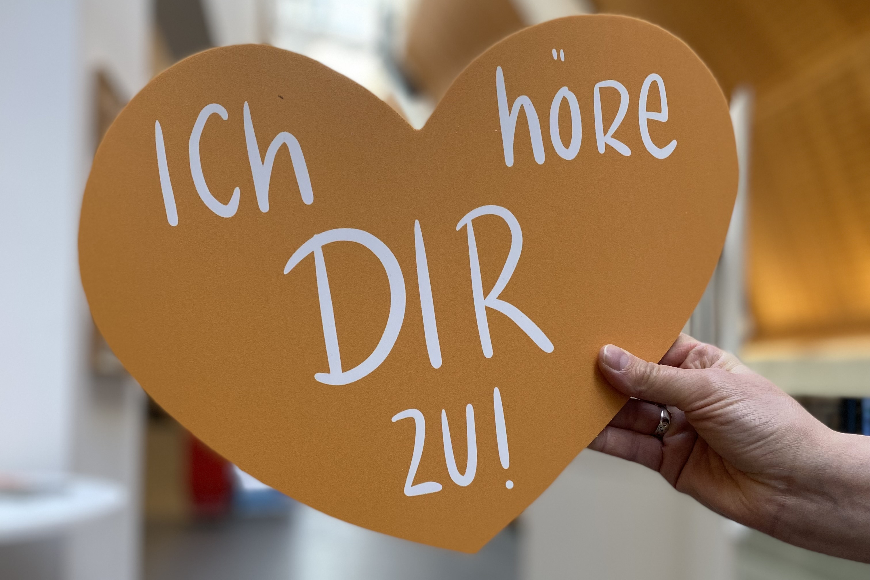 Eine Hand hält ein Herz. Darauf steht der Satz: Ich höre dir zu.