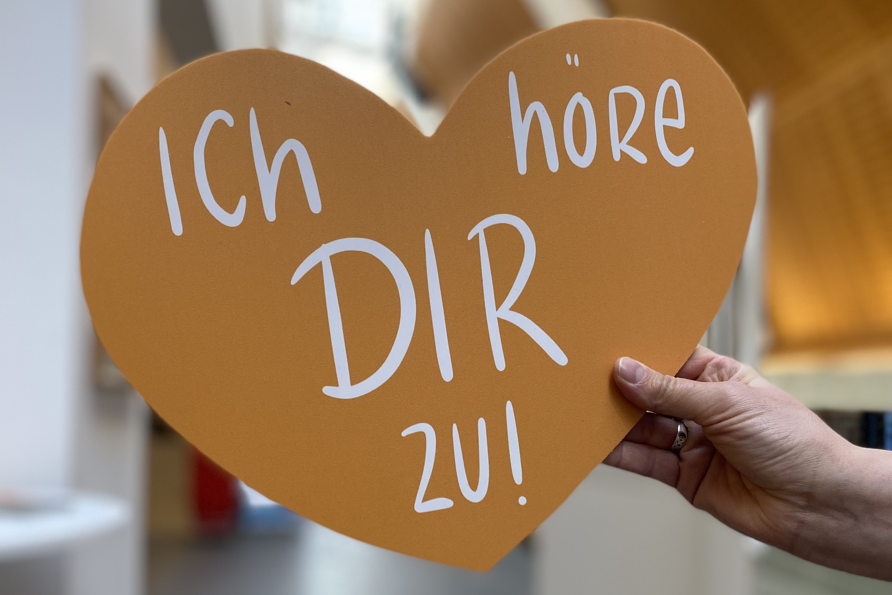 Eine Hand hält ein Herz. Darauf steht der Satz: Ich höre dir zu.