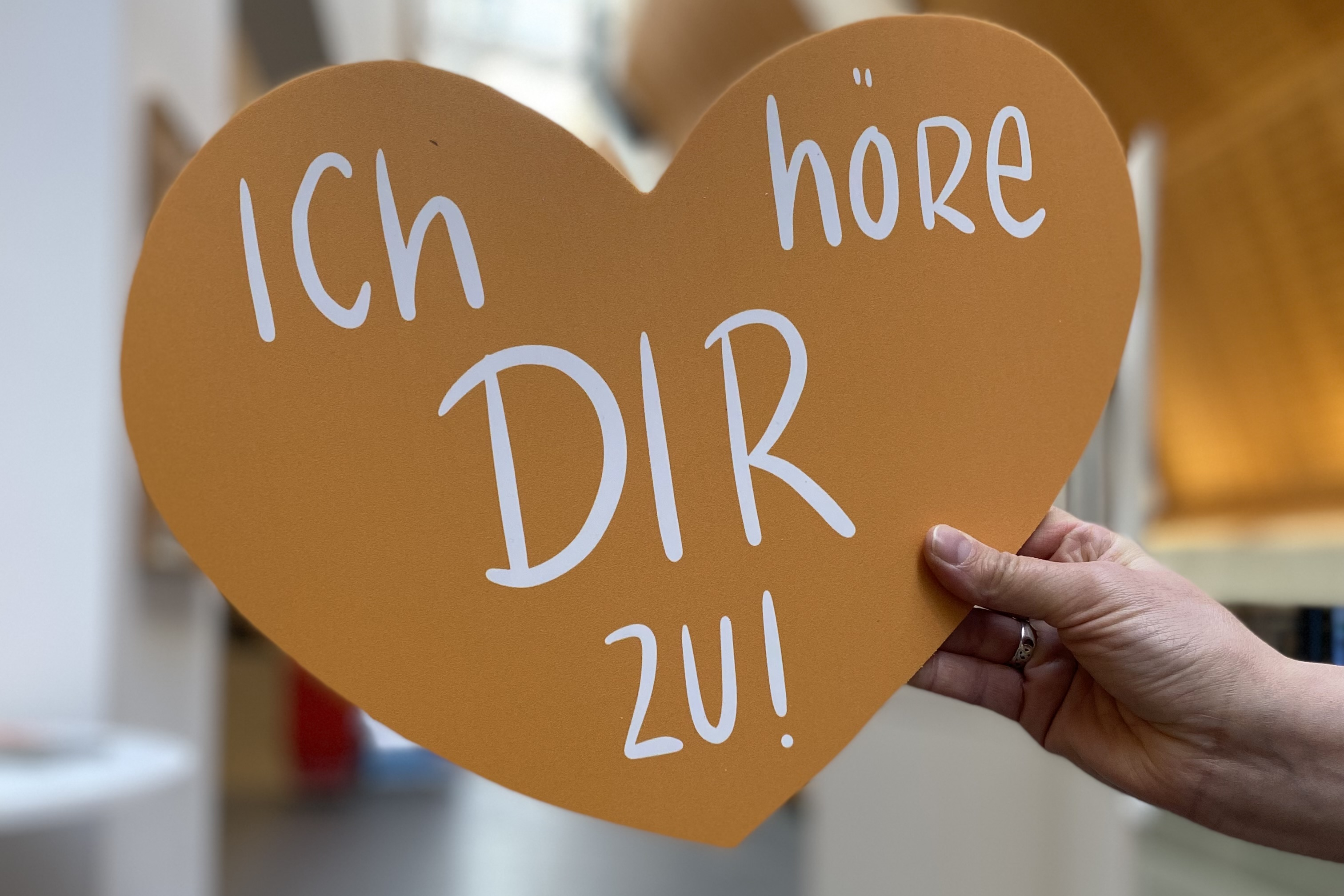 Eine Hand hält ein Herz. Darauf steht der Satz: Ich höre dir zu.