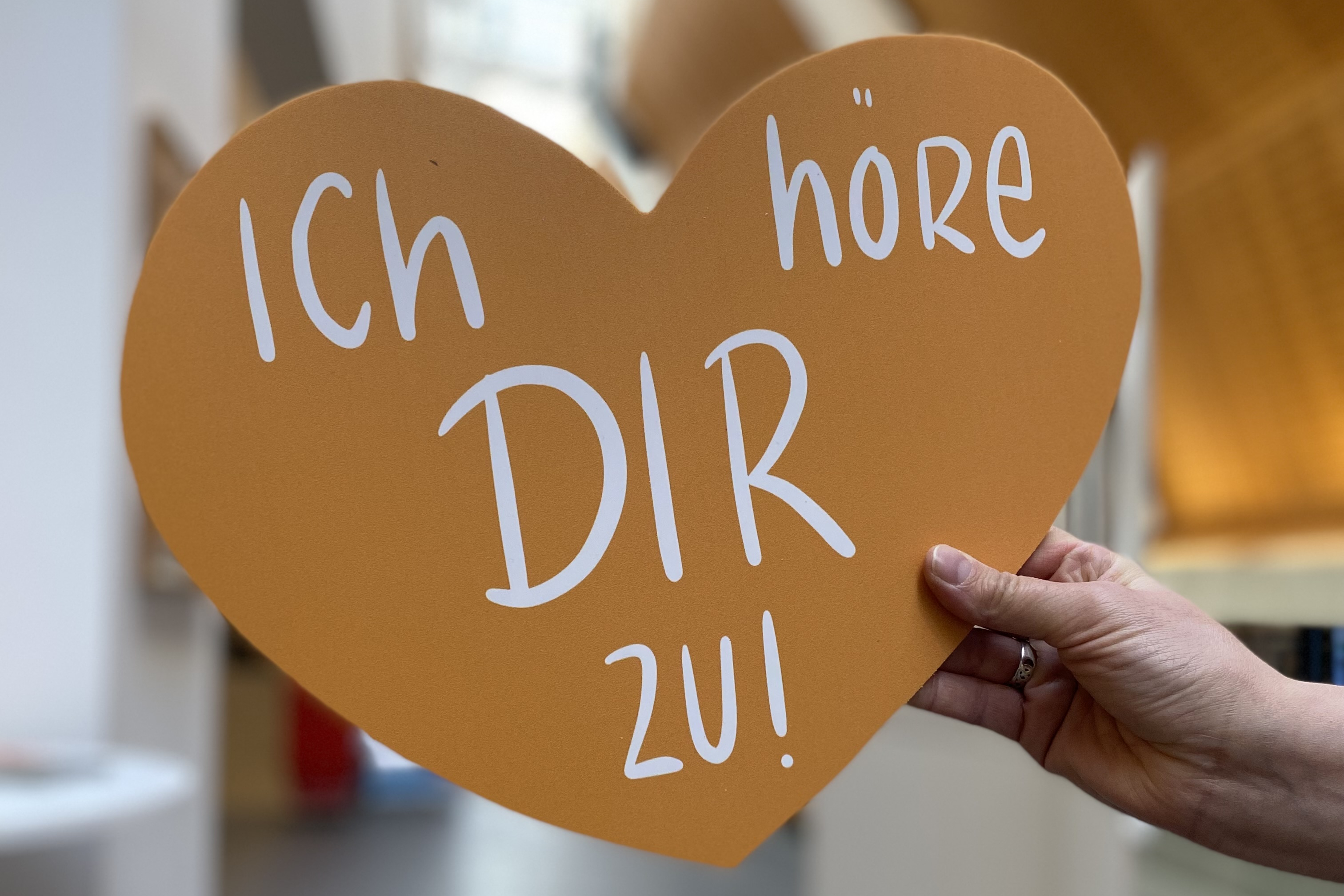 Eine Hand hält ein Herz. Darauf steht der Satz: Ich höre dir zu.