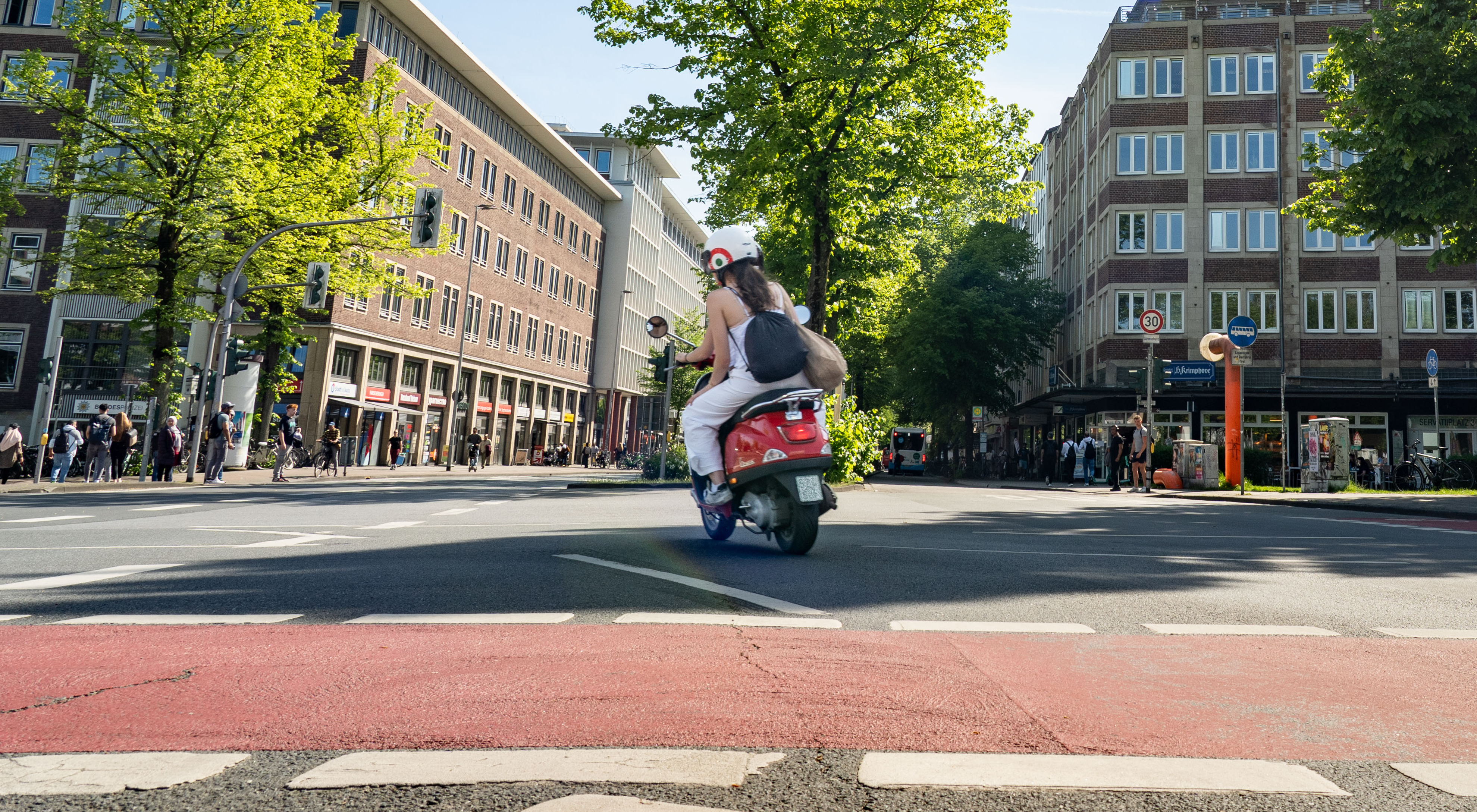 Eine Rollerfahrerin fährt im Sommer über die Kreuzung am Servatiiplatz