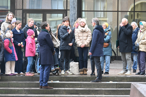 Eine Gruppe Jugendlicher steht mit zwei Erwachsenen auf einer Treppe. Einer der Jugendlichen hat ein Mirkofon in der Hand und spricht hinein.