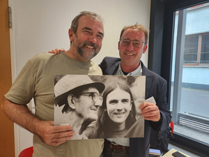Zwei Personen halten ein großformatiges schwarz-weiß-Foto mit ebenfalls zwei Personen.
