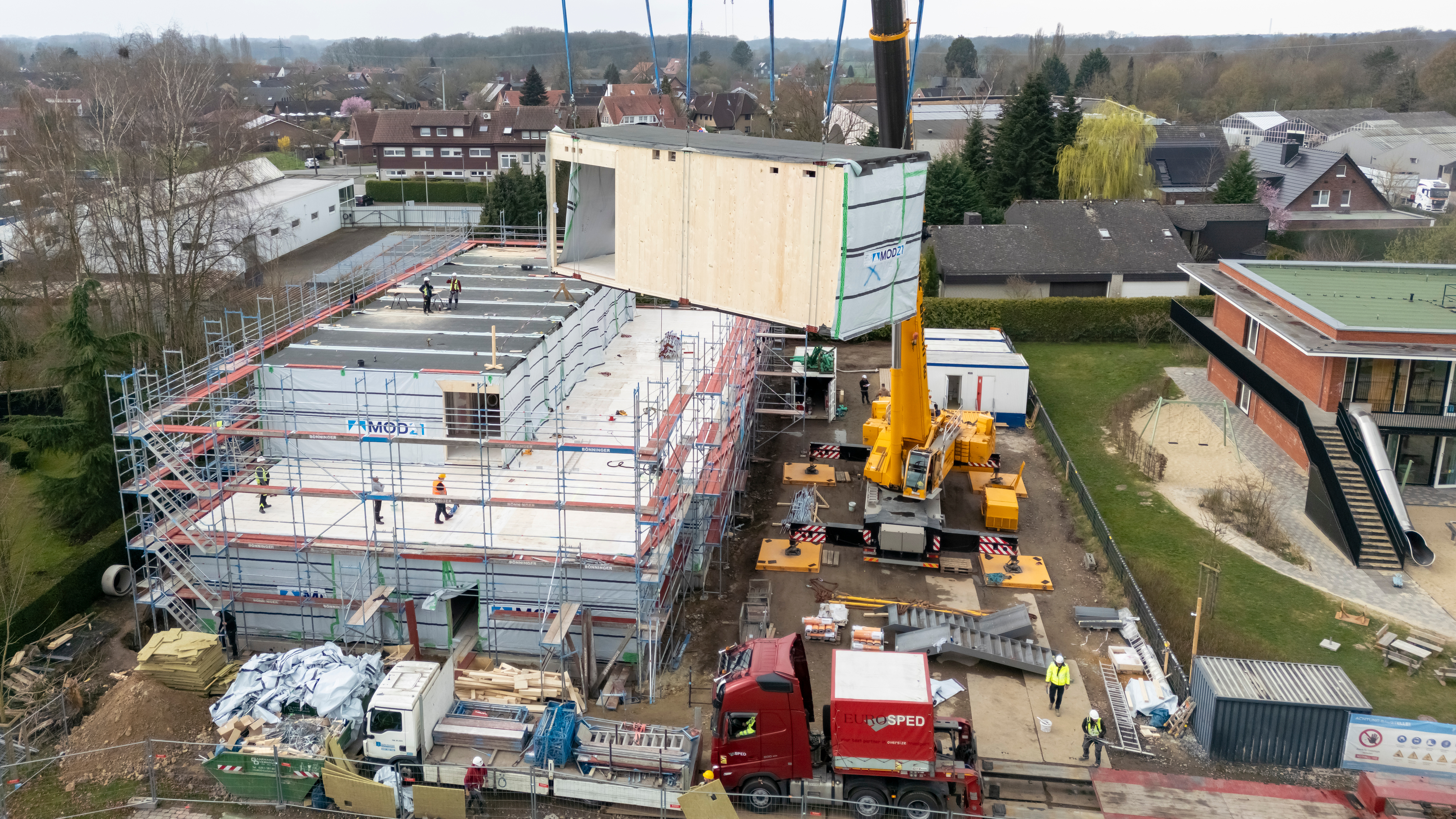 Eines der Module schwebt hängend am Baustellenkran über der Baustelle
