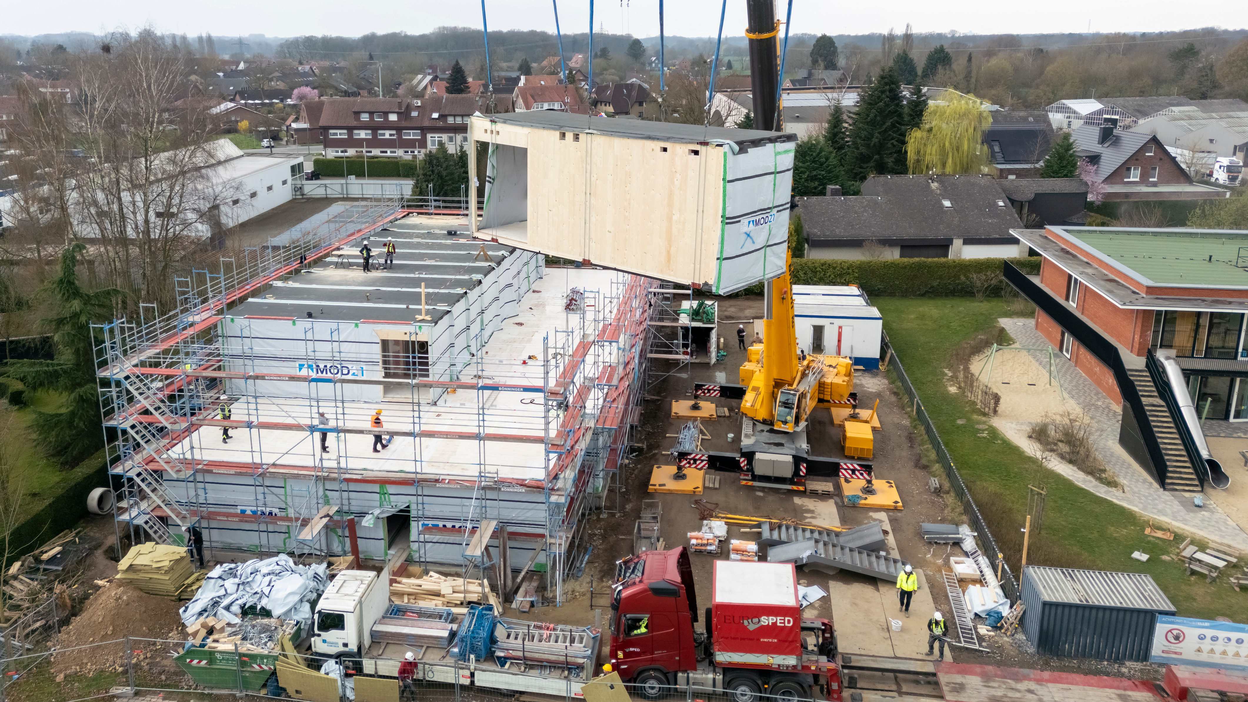 Eines der Module schwebt hängend am Baustellenkran über der Baustelle
