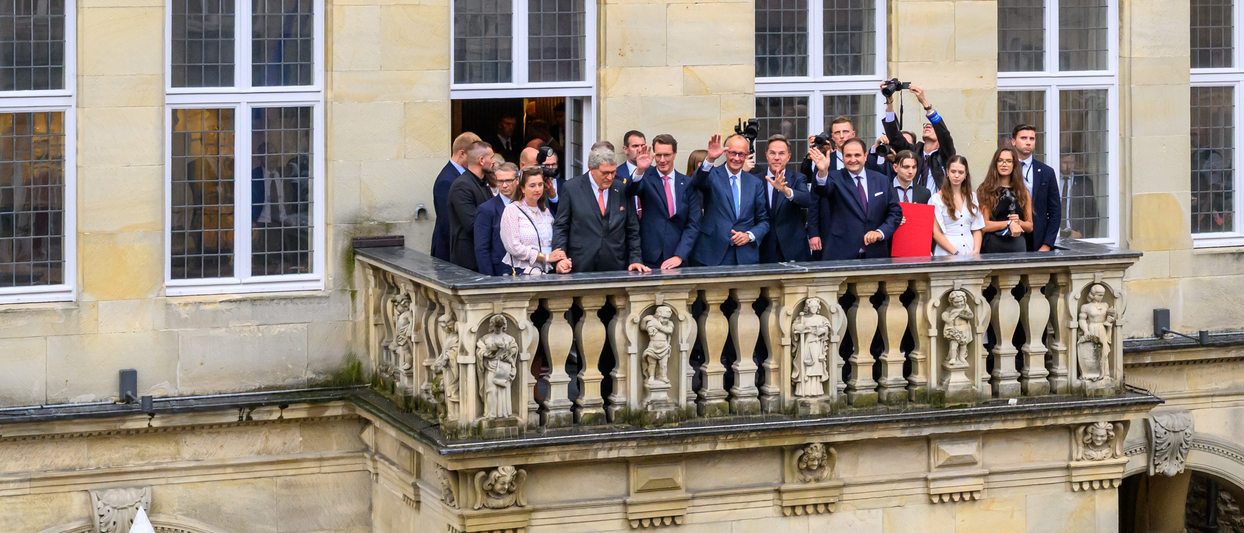 Mehrere Menschen stehen auf dem Sentenzbogen am Stadtweinhaus und Winken ins Publikum.