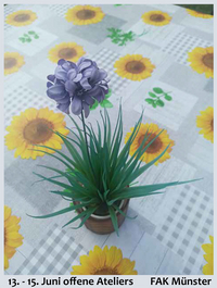 Fotografie von Gertrud Neuhaus, auf der eine Topfpflanze auf einer Tischdecke mit Sonnenblumenmuster steht.