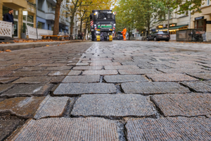 Auf dem Bild ist Kopfsteinpflaster abgebildet, das zum Teil unbehandelt ist und zum anderen Teil aufgrund einer Fräsmaschine abgefräst worden ist. Man testet das Grindingverfahren, das hilft, die Straßen zu verbessern, ohne den historischen Charakter des Kopfsteinpflasters zu verändern oder zu asphaltieren. 