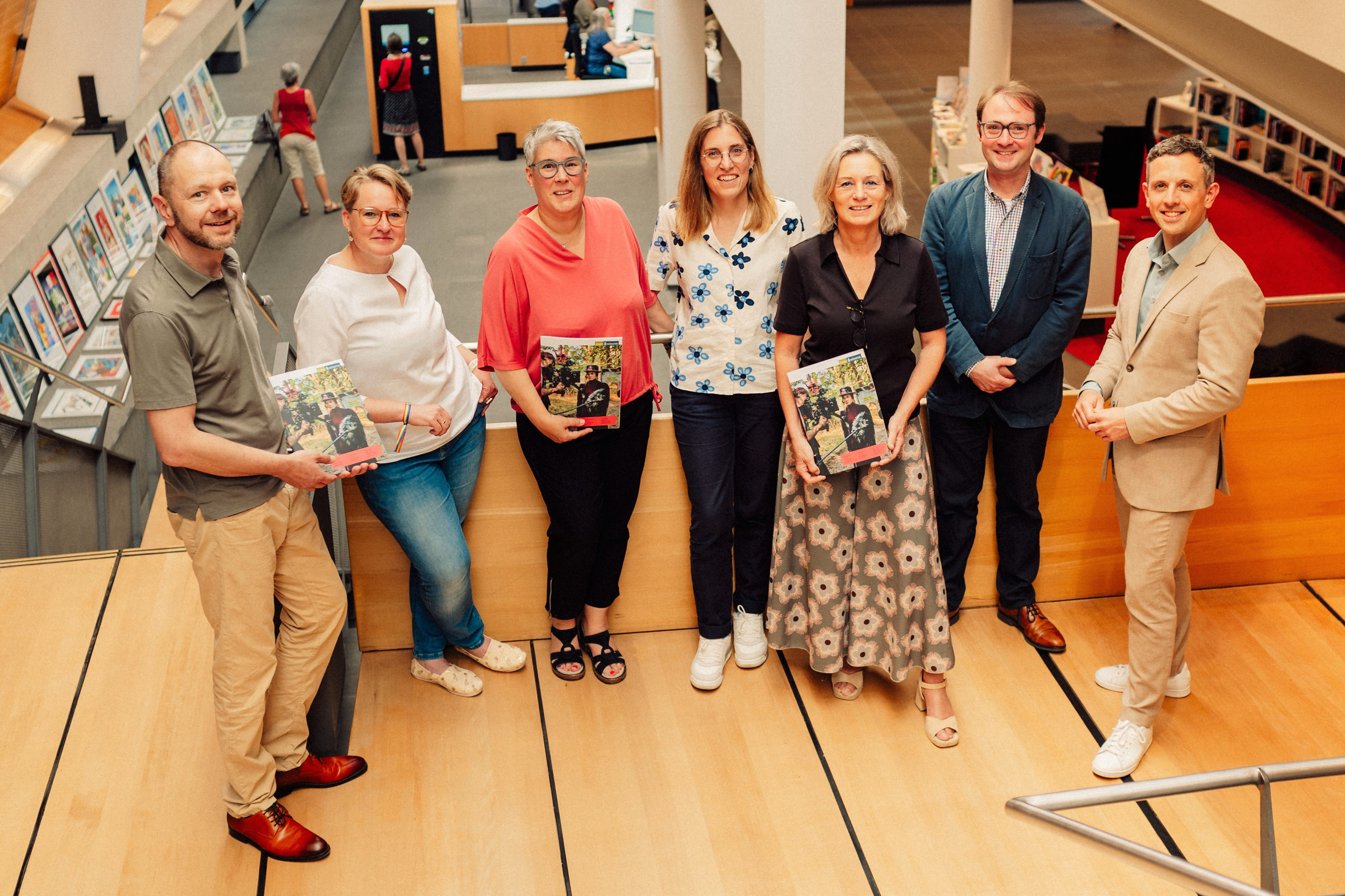 Auf einem Treppenabsatz in der Stadtbücherei stehen sieben Personen, manche halten das Kulturmagazin in den Händen.