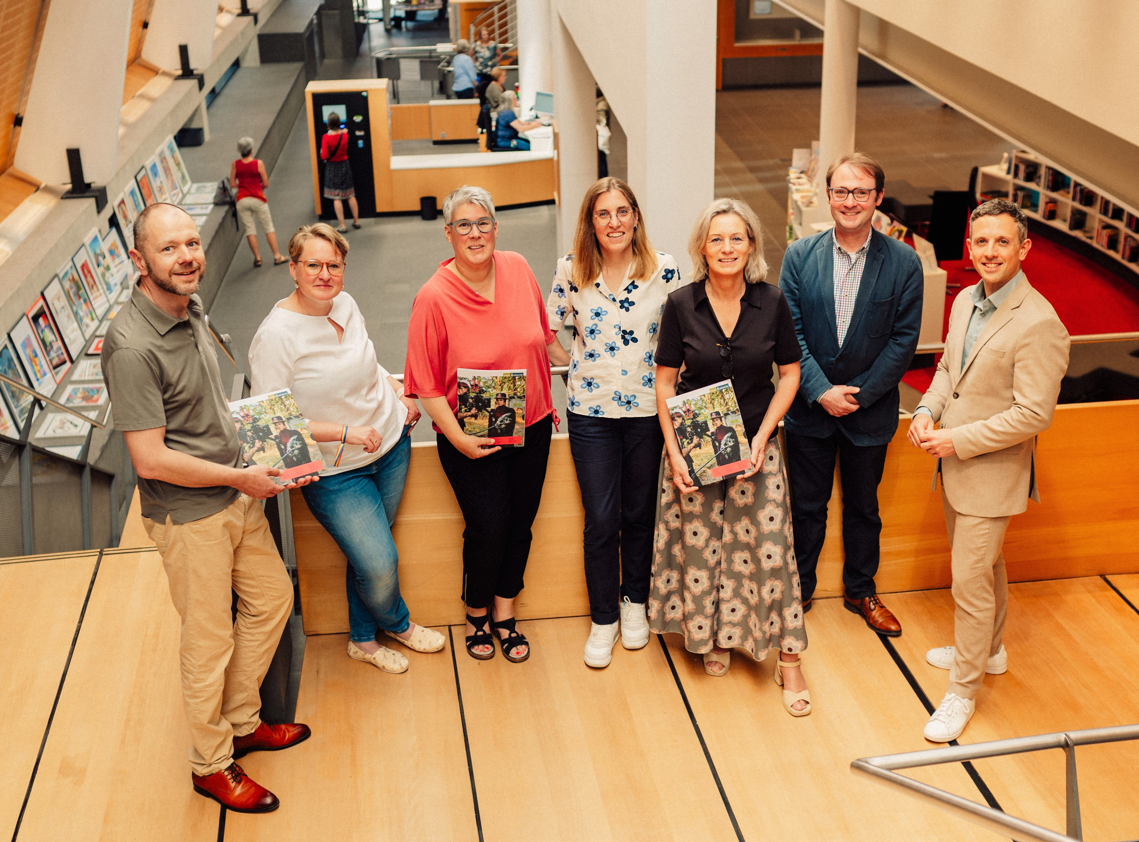 Auf einem Treppenabsatz in der Stadtbücherei stehen sieben Personen, manche halten das Kulturmagazin in den Händen.
