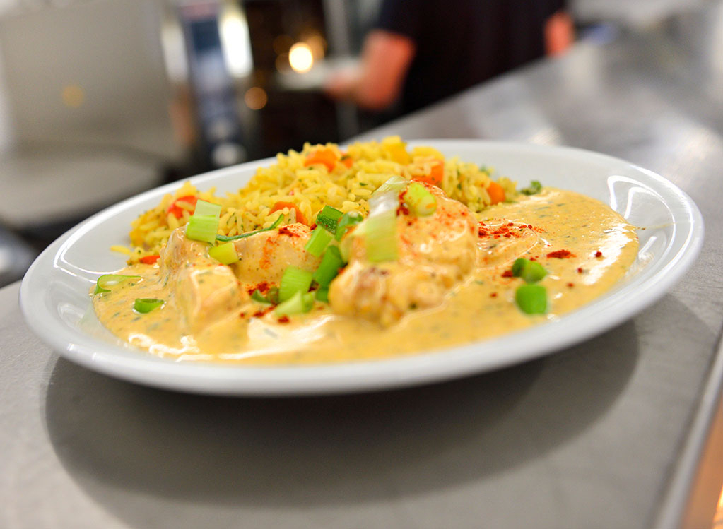Ein Teller mit einem Mittagessen steht auf einer Theke, im Hintergrund ist ein Mitarbeiter zu sehen.