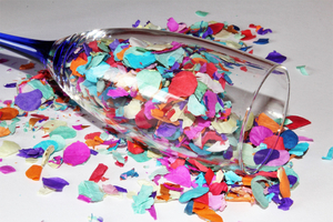 Ein Sektglas liegt umgefallen auf einem Tisch. Darin und rundherum befindet sich buntes Konfetti.