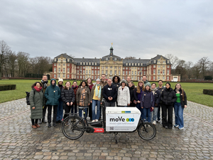 Gruppenbild, Studierende stehen vor dem Universitätsschloss, ein Fahrrad im Vordergrund 