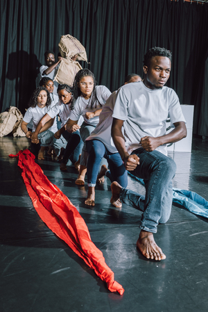 Junge Menschen hocken hintereinander auf einer Theaterbühne.