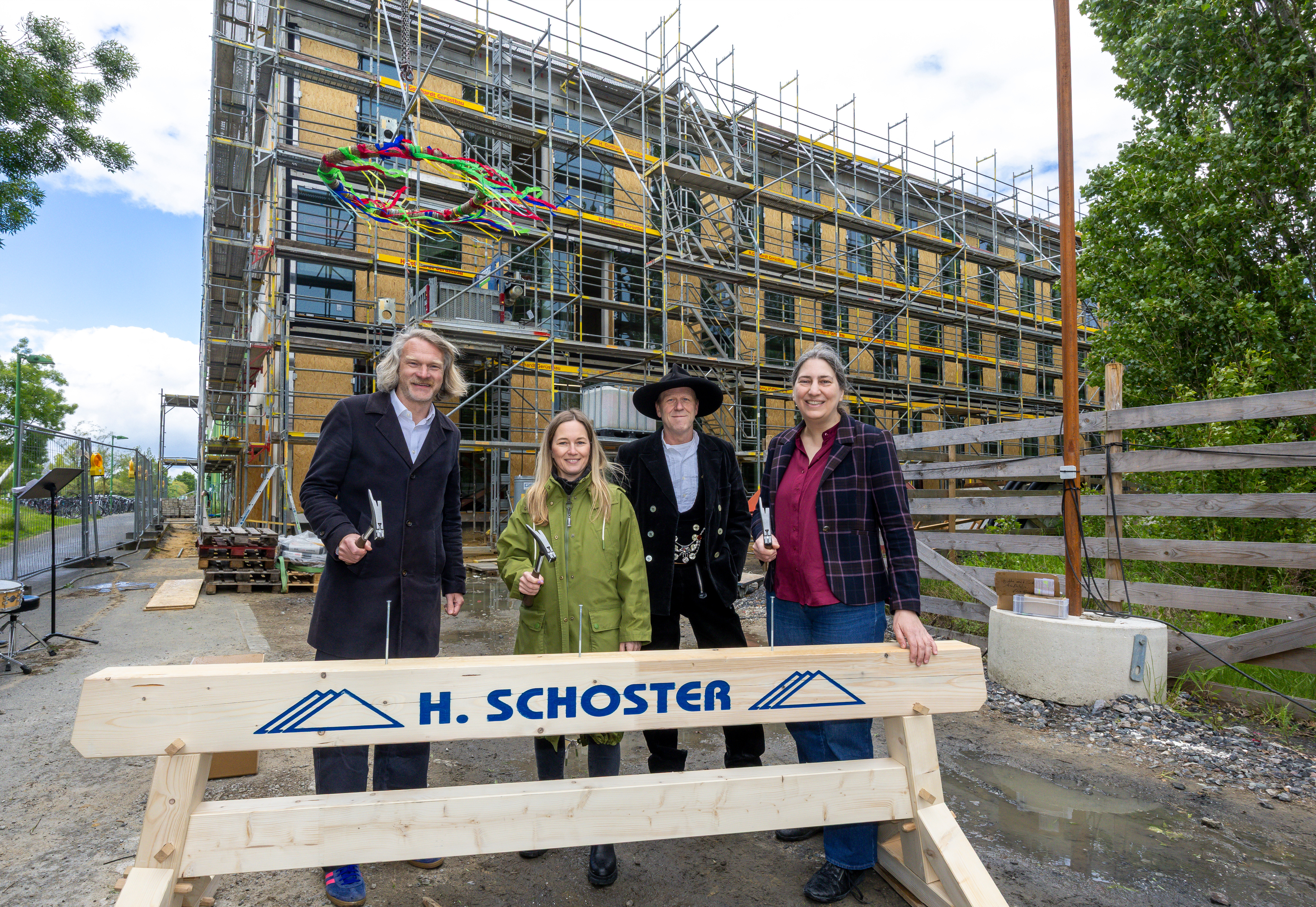 Vier Personen hinter einem Holzbalken stehen vor dem Erweiterungsbau