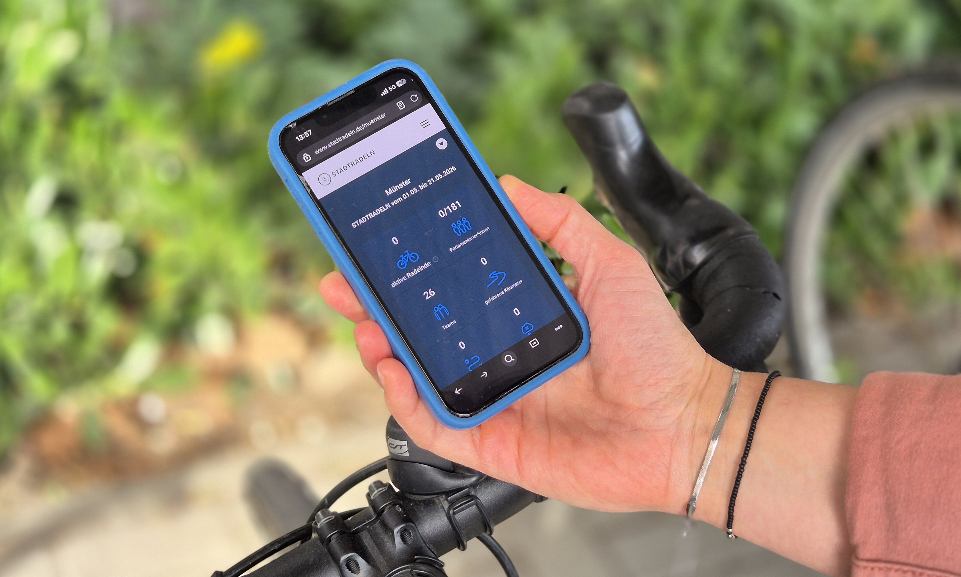 Eine Hand hält ein Handy in der Hand, auf dem die Stadtradeln-App geöffnet ist. Im Hintergrund ein Fahrradlenker.