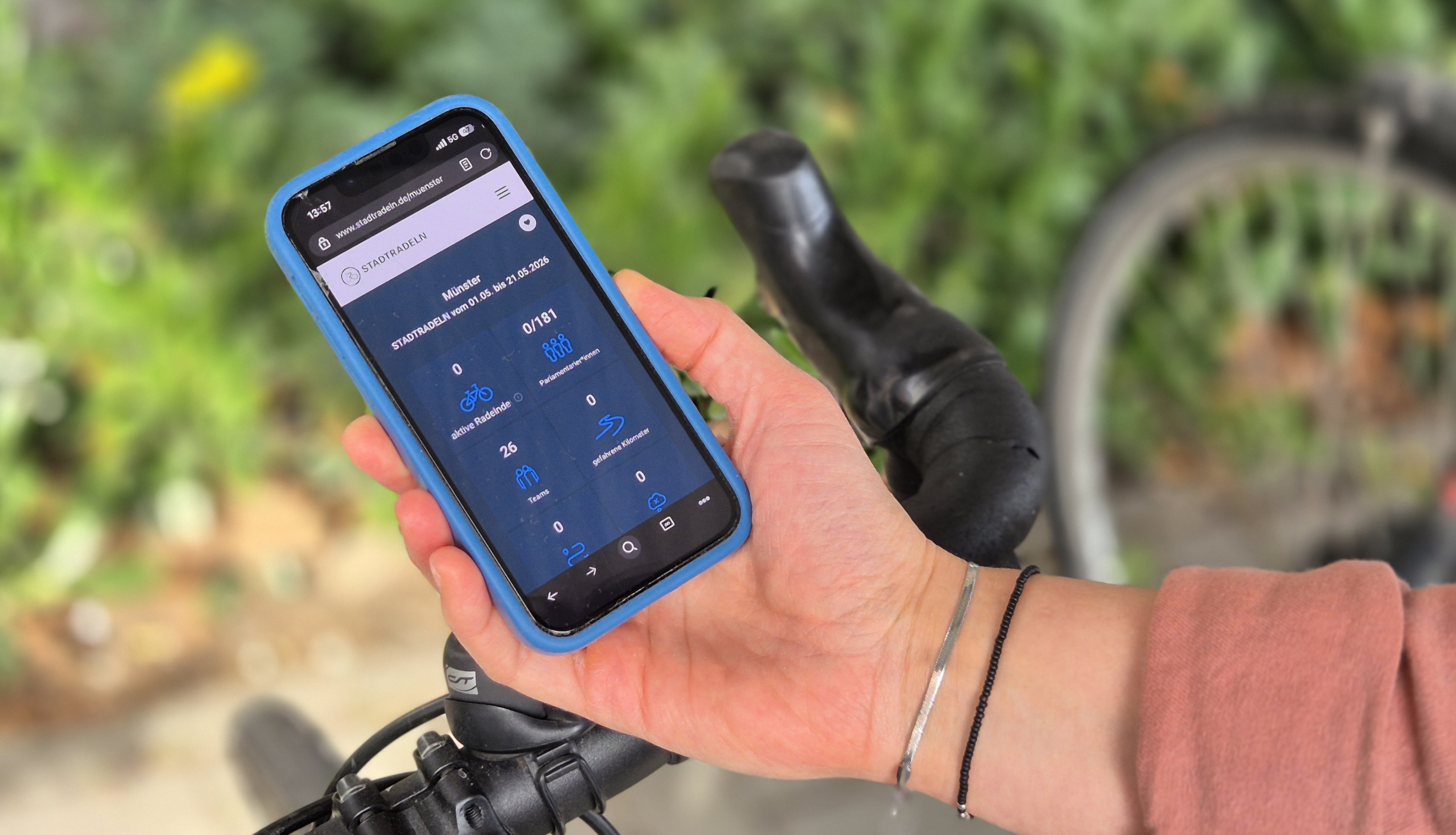 Eine Hand hält ein Handy in der Hand, auf dem die Stadtradeln-App geöffnet ist. Im Hintergrund ein Fahrradlenker.