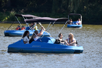 Auf dem Foto ist eine Gruppe Menschen beim Tretbootfahren auf dem Aasee zu sehen. Insgesamt sind drei blaue Tretboote mit Sonnendach bzw. -segel zu sehen, eines davon im Vordergrund.