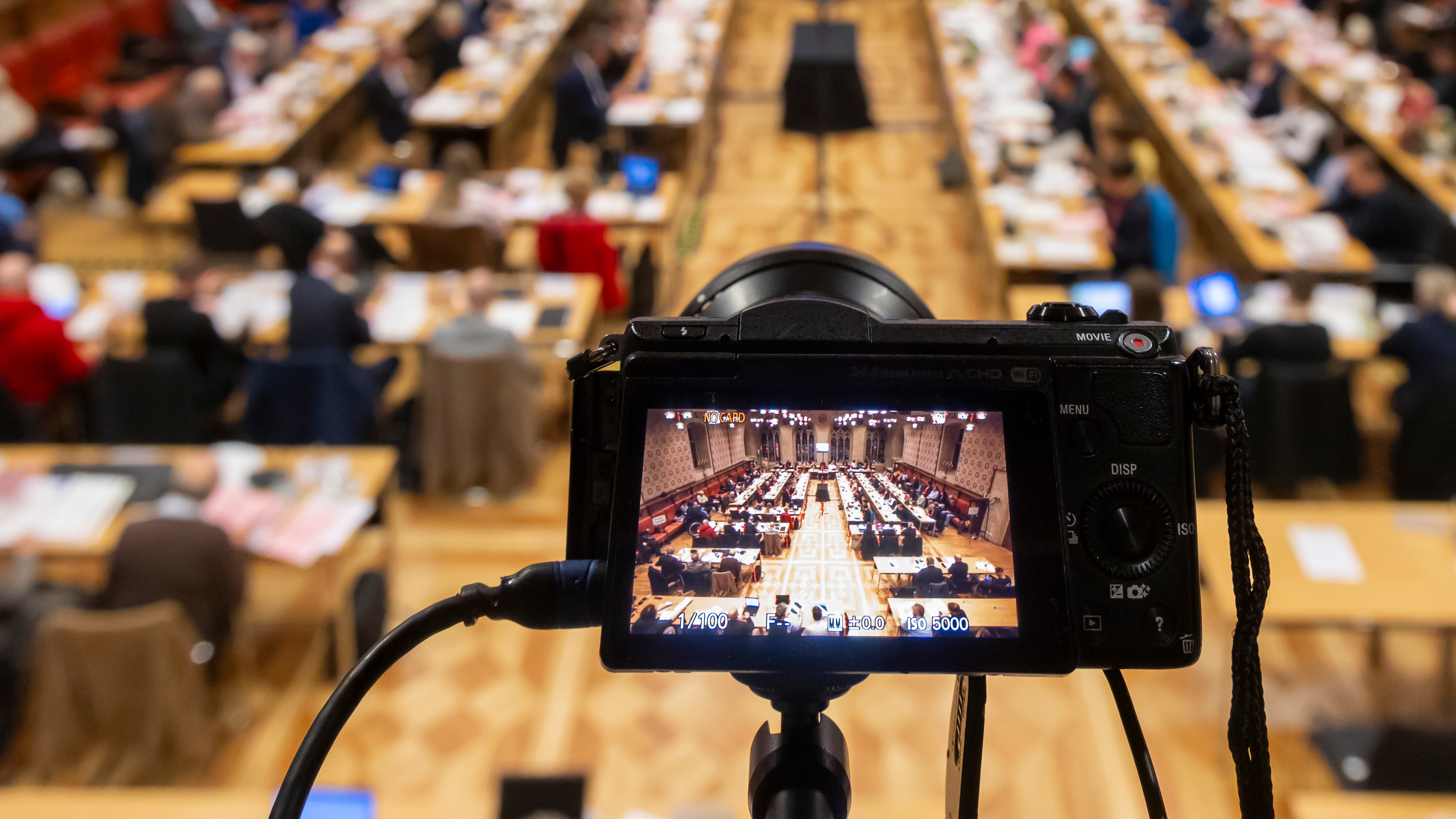 Blick auf die Ratssitzung im Rathausfestsaal, im Vordergrund eine Kamera, die ebenfalls auf die Sitzung gerichtet ist.