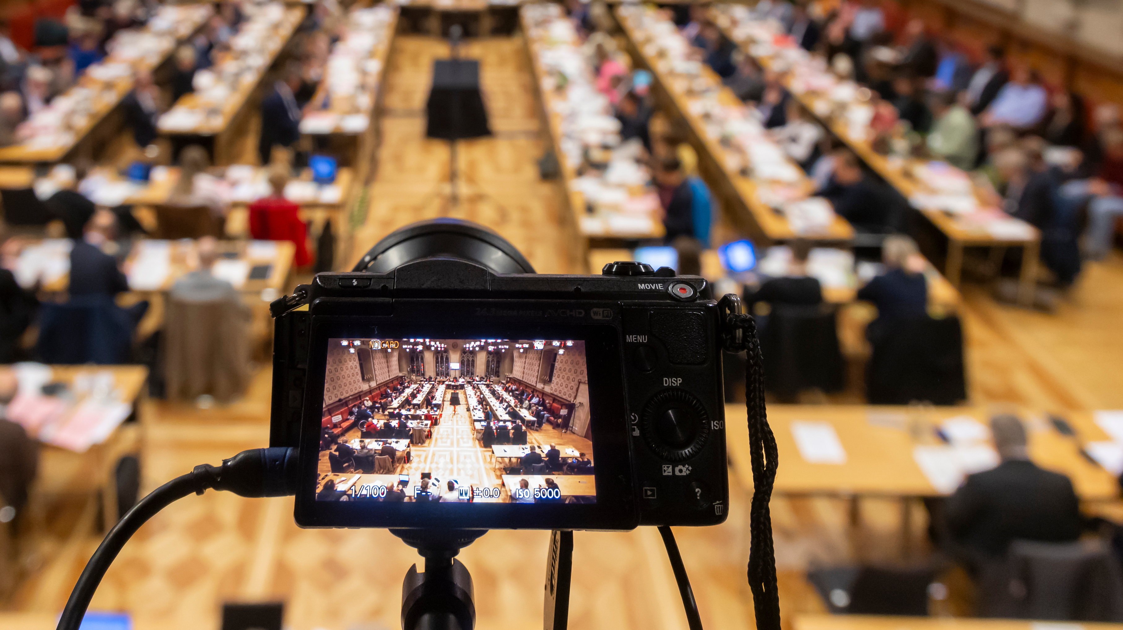 Blick auf die Ratssitzung im Rathausfestsaal, im Vordergrund eine Kamera, die ebenfalls auf die Sitzung gerichtet ist.
