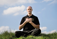 Der Dozent Volker Nowak-von der Way sitzt in meditierender Haltung auf einer Wiese