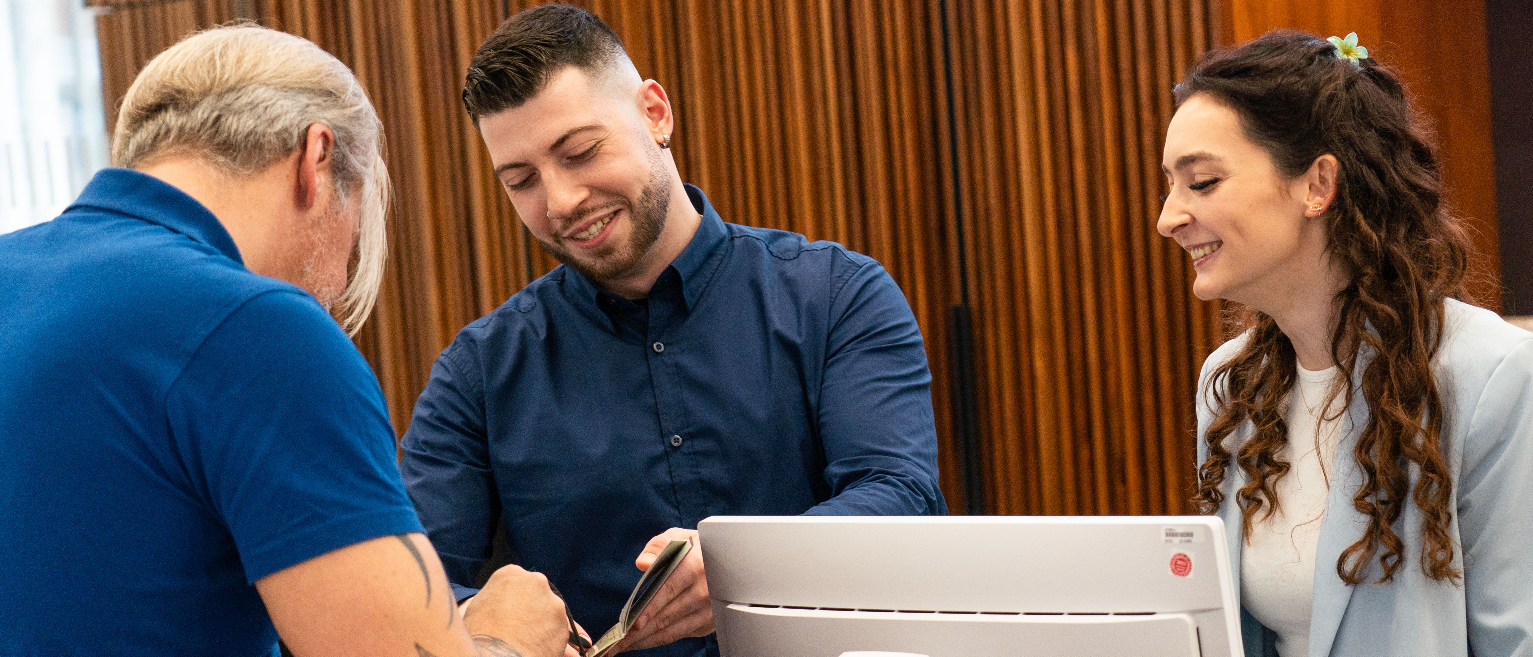 Zwei Personen stehen hinter einer Servicetheke und geben einem Mann vor der Theke Auskunft.